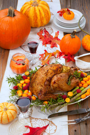 Citrus glazed roasted Turkey for Thanksgiving celebration garnished with kumquat, raspberry, asparagus, oregano, and fresh rosemary twigs. Red wine, side dishes, and gravy. Holiday table decorated with pumpkins, candels, gourds, and fall leaves.の写真素材
