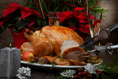 Carving garnished roasted Christmas turkey with grab apples, sweet chestnut, cranberry, Christmas ornaments, candles, and pine cones.の写真素材