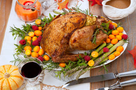 Citrus glazed roasted Turkey for Thanksgiving celebration garnished with kumquat, raspberry, asparagus, oregano, and fresh rosemary twigs. Red wine, side dishes, and gravy.の写真素材