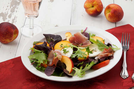 Closeup of Prosciutto peach salad with fresh Mozzarella plate mixed with spring greens. Fresh peaches.の写真素材