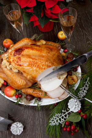 Carving garnished roasted Christmas turkey with grab apples, sweet chestnut, cranberry, Christmas ornaments, candles, and pine cones.の写真素材