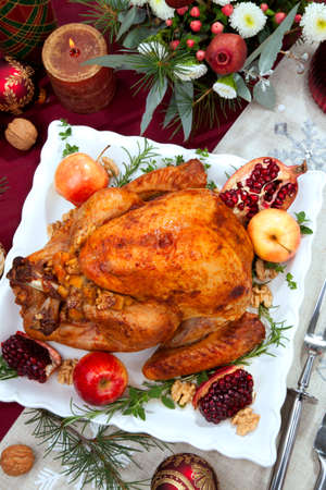 Pomegranate glazed roasted turkey on a tray garnished with fresh pomegranates, apples, herbs, and walnuts on Christmas-decorated table with candles, ornaments, fir twigs and flutes of champagne.の写真素材
