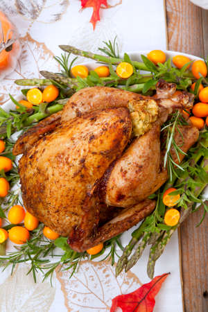 Citrus glazed roasted Turkey for Thanksgiving celebration garnished with kumquat, raspberry, asparagus, oregano, and fresh rosemary twigs. Red wine, side dishes, and gravy. Holiday table decorated with pumpkins, candels, gourds, and fall leaves.の写真素材