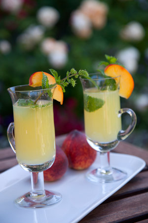 Closeup of Peach Mojito garnished with peach wedge and twig of mint. Outside cocktails / drinks in a garden.の写真素材