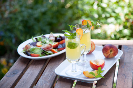 Closeup of Peach Mojito garnished with peach wedge and twig of mint and green peach salad. Outside cocktails / drinks in a garden.の写真素材