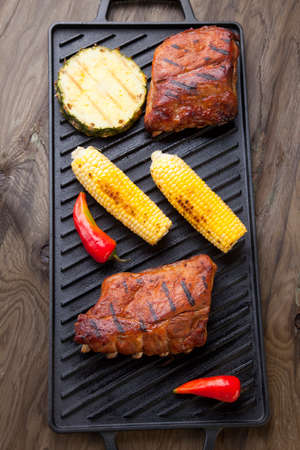 Grilled pork ribs on griddle with chili pepper, cherry tomatoes, and grilled cornの写真素材