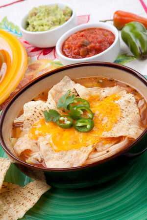 Closeup of a bowl of hot delicious spicy chicken nacho soup, garnished with melted cheese, jalapeno pepper, and fresh cilantro. Salsa, guacamole, and marinated hot pepper.の写真素材