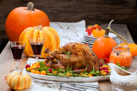 Citrus glazed roasted Turkey for Thanksgiving celebration garnished with kumquat, raspberry, asparagus, oregano, and fresh rosemary twigs. Red wine, side dishes, and gravy. Holiday table decorated with pumpkins, candels, gourds, and fall leaves.の写真素材