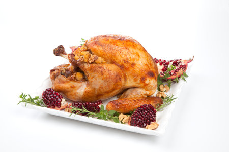 Pomegranate glazed roasted turkey on a tray garnished with fresh pomegranates, herbs, and walnuts over white background.の写真素材