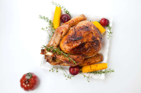 Garnished traditional fall roasted turkey garnished with corn on the cob, plums, and herbs. On white background with pumpkins.の写真素材