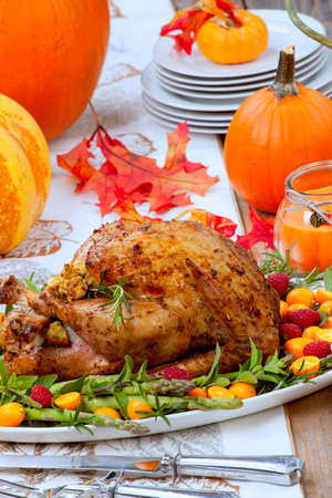 Citrus glazed roasted Turkey for Thanksgiving celebration garnished with kumquat, raspberry, asparagus, oregano, and fresh rosemary twigs. Red wine, side dishes, and gravy. Holiday table decorated with pumpkins, candels, gourds, and fall leaves.の写真素材
