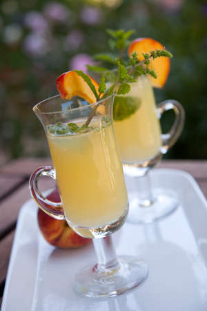 Closeup of Peach Mojito garnished with peach wedge and twig of mint. Outside cocktails / drinks in a garden.の写真素材