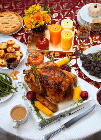 Garnished traditional fall roasted turkey garnished with corn on the cob, plums, and herbs. Served on a traditional decorated table with pumpkins, pie, green beans, baked vegetables, cranberry relish, corn bread, red wine, flowers, and candles.の写真素材