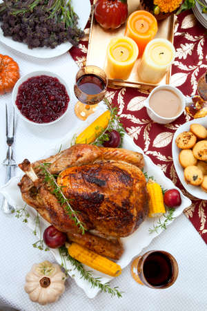 Garnished traditional fall roasted turkey garnished with corn on the cob, plums, and herbs. Served on a traditional decorated table with pumpkins, pie, green beans, baked vegetables, cranberry relish, corn bread, red wine, flowers, and candles.の写真素材