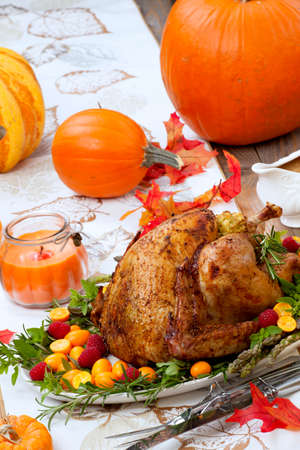 Citrus glazed roasted Turkey for Thanksgiving celebration garnished with kumquat, raspberry, asparagus, oregano, and fresh rosemary twigs. Red wine, side dishes, and gravy. Holiday table decorated with pumpkins, candels, gourds, and fall leaves.の写真素材