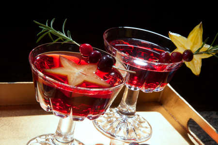Closeup of star fruit martini garnished with fresh cranberry and rosemary, on a tray with Christmas ornaments. Holiday cocktails series.の写真素材