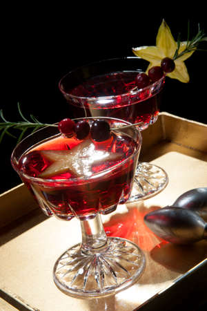 Closeup of star fruit martini garnished with fresh cranberry and rosemary, on a tray with Christmas ornaments. Holiday cocktails series.の写真素材