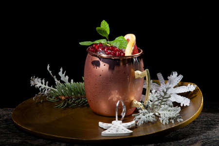 Closeup of Christmas pomegranate Moscow Mule garnished with fresh pomegranate, mint, and slice of grapefruit on a tray with Christmas ornaments. Holiday cocktails series.の写真素材