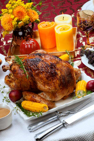 Garnished traditional fall roasted turkey garnished with corn on the cob, plums, and herbs. Served on a traditional decorated table with pumpkins, pie, green beans, baked vegetables, cranberry relish, corn bread, red wine, flowers, and candles.の写真素材