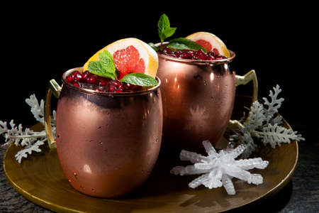 Closeup of Christmas pomegranate Moscow Mule garnished with fresh pomegranate, mint, and slice of grapefruit on a tray with Christmas ornaments. Holiday cocktails series.の写真素材