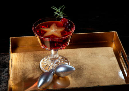 Closeup of star fruit martini garnished with fresh cranberry and rosemary, on a tray with Christmas ornaments. Holiday cocktails series.の写真素材