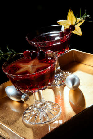 Closeup of star fruit martini garnished with fresh cranberry and rosemary, on a tray with Christmas ornaments. Holiday cocktails series.の写真素材