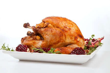 Pomegranate glazed roasted turkey on a tray garnished with fresh pomegranates, herbs, and walnuts over white background.の写真素材