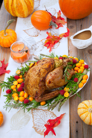 Citrus glazed roasted Turkey for Thanksgiving celebration garnished with kumquat, raspberry, asparagus, oregano, and fresh rosemary twigs. Red wine, side dishes, and gravy. Holiday table decorated with pumpkins, candels, gourds, and fall leaves.の写真素材