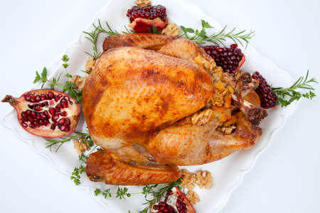 Pomegranate glazed roasted turkey on a tray garnished with fresh pomegranates, herbs, and walnuts over white background.の写真素材