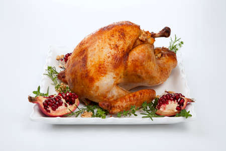 Pomegranate glazed roasted turkey on a tray garnished with fresh pomegranates, herbs, and walnuts over white background.の写真素材