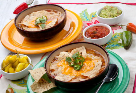 Closeup of two bowls of hot delicious spicy chicken nacho soup, garnished with melted cheese, jalapeno pepper, and fresh cilantro. Salsa, guacamole, and marinated hot pepper.の写真素材