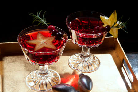 Closeup of star fruit martini garnished with fresh cranberry and rosemary, on a tray with Christmas ornaments. Holiday cocktails series.の写真素材