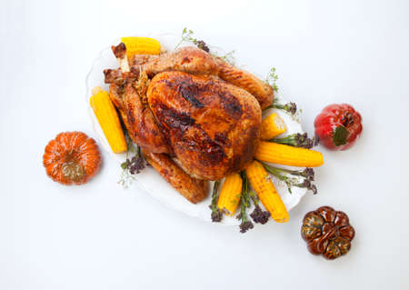 Garnished traditional fall roasted turkey garnished with corn on the cob, plums, and herbs. On white background with pumpkins.の写真素材
