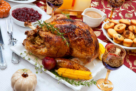 Garnished traditional fall roasted turkey garnished with corn on the cob, plums, and herbs. Served on a traditional decorated table with pumpkins, pie, green beans, baked vegetables, cranberry relish, corn bread, red wine, flowers, and candles.の写真素材