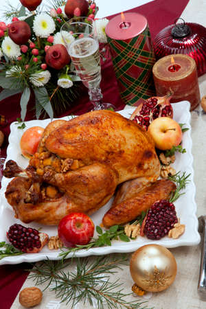 Pomegranate glazed roasted turkey on a tray garnished with fresh pomegranates, apples, herbs, and walnuts on Christmas-decorated table with candles, ornaments, fir twigs and flutes of champagne.の写真素材