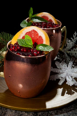 Closeup of Christmas pomegranate Moscow Mule garnished with fresh pomegranate, mint, and slice of grapefruit on a tray with Christmas ornaments. Holiday cocktails series.の写真素材