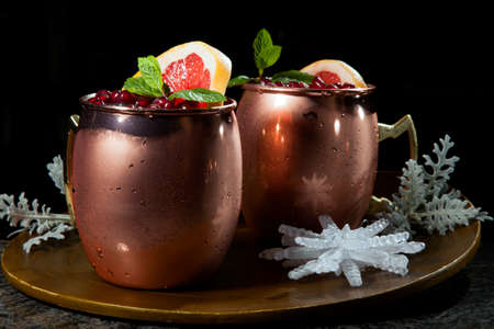Closeup of Christmas pomegranate Moscow Mule garnished with fresh pomegranate, mint, and slice of grapefruit on a tray with Christmas ornaments. Holiday cocktails series.の写真素材