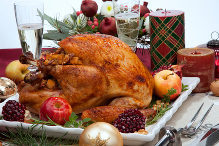 Pomegranate glazed roasted turkey on a tray garnished with fresh pomegranates, apples, herbs, and walnuts on Christmas-decorated table with candles, ornaments, fir twigs and flutes of champagne.の写真素材