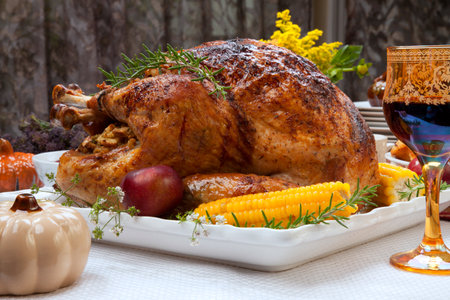 Garnished traditional fall roasted turkey garnished with corn on the cob, plums, and herbs. Served on a traditional decorated table with pumpkins, pie, green beans, baked vegetables, cranberry relish, corn bread, red wine, flowers, and candles.の写真素材