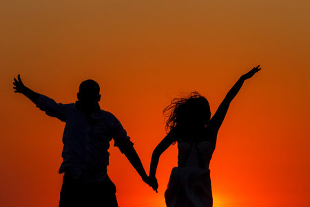 lovers silhouetted against a setting sun on the beachの写真素材