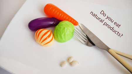 children's artificial vegetables, fork and knife, lie on a white plate on a white background, the inscriptionの写真素材