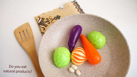 children's artificial vegetables, lie in a frying pan, on a napkin, wooden spatula, on a white background, the inscriptionの写真素材