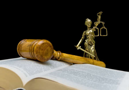Statue of justice on a black background. Gavel and law book in the foreground out of focus.の写真素材