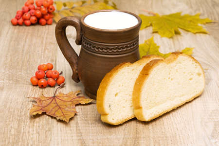 Fresh bread and milk in a clay mug close-up on wooden boardsの写真素材
