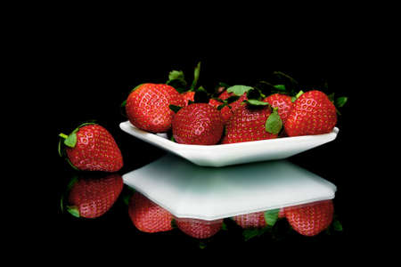 ripe juicy strawberries on a plate on a black background with mirror reflection. horizontal photo.の写真素材