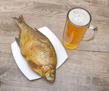 appetizing smoked bream and a glass of light beer on a wooden table. の写真素材