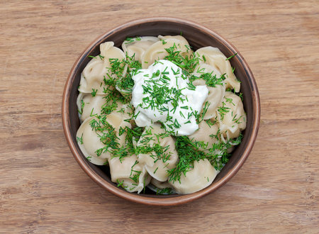 Russian dumplings with dill and sour cream in a clay bowl on a wooden background. horizontal photo.の写真素材