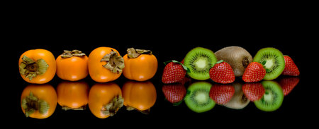 persimmon, kiwi and strawberries on a black background. horizontal photo.の写真素材