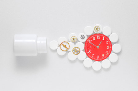 White pills and red clock on a white background with gearsの写真素材