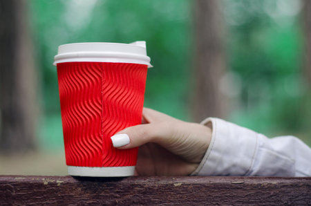 Female hand bench a cup of coffee green treesの写真素材